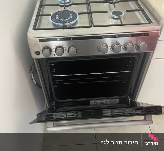 תנור גז עם ארבעה מבערים דולקים ודלת פתוחה